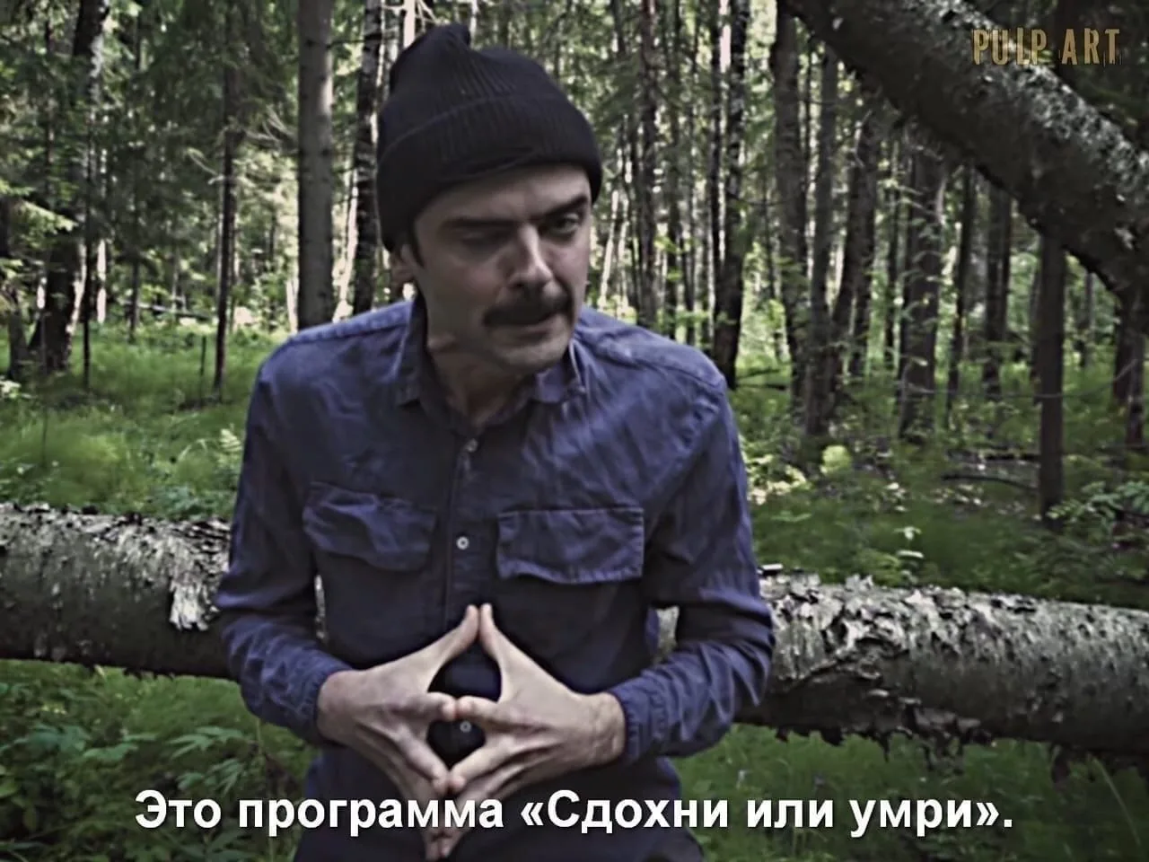 Кадр из леса: человек в шапке сложил пальцы домиком, подпись «Это программа „Сдохни или умри“»